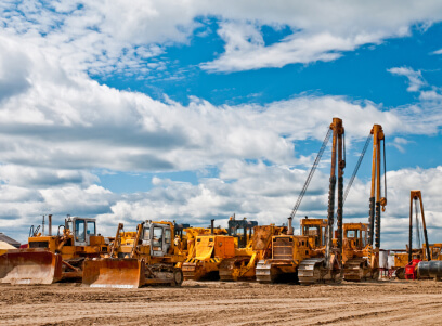 A group of construction equipment parked in the dirt.