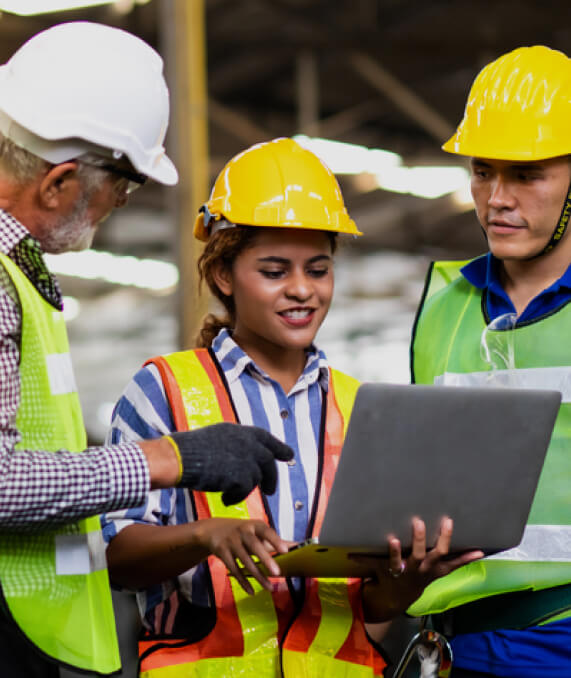 A group of people in hard hats and vests looking at something on a laptop.